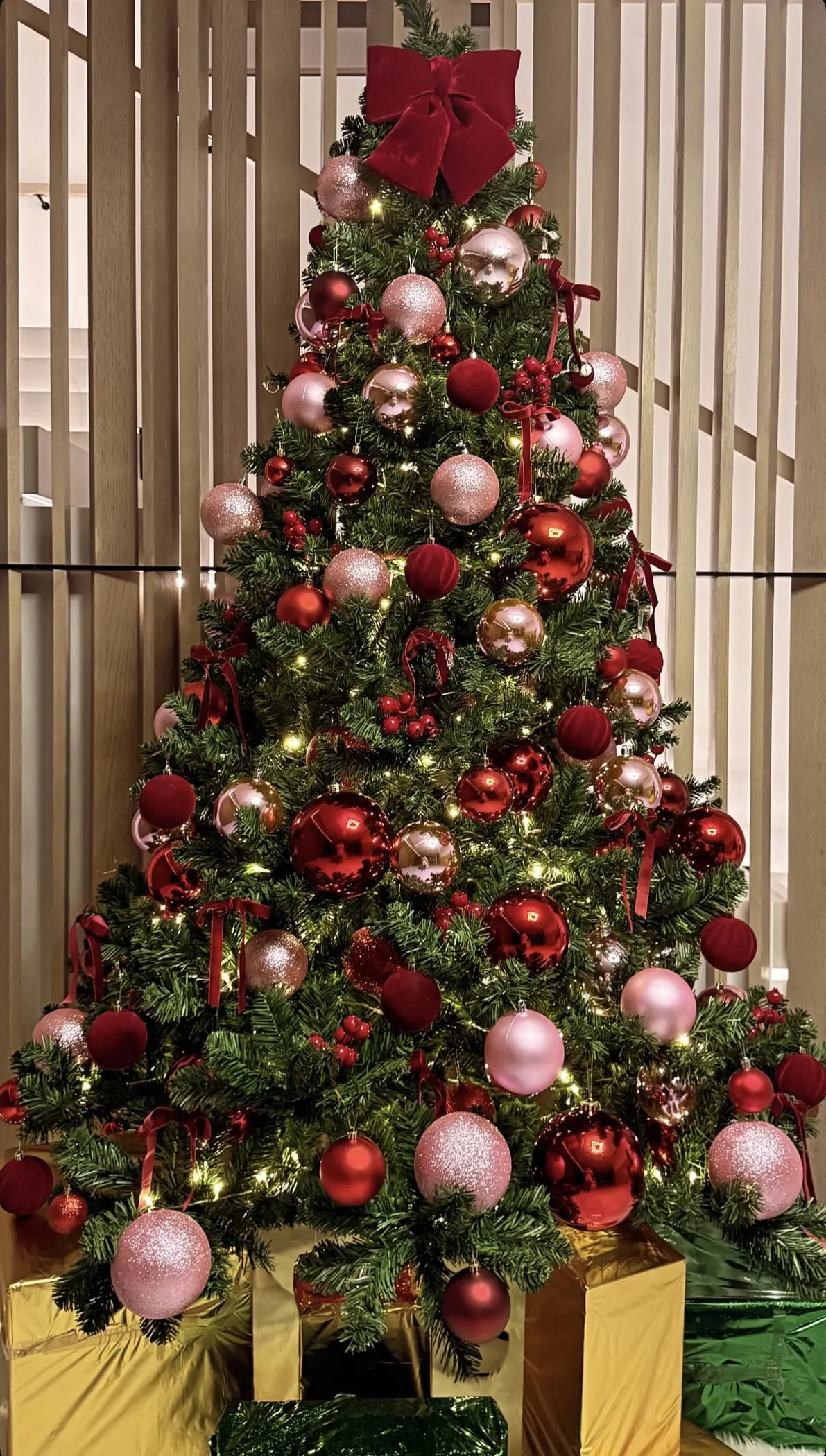 A tree dressed in blush pink and red baubles with a red velvet bow on top